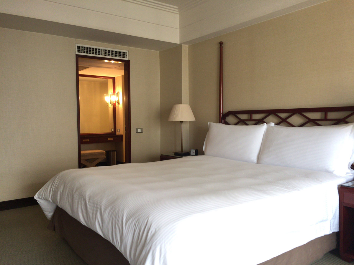 ベッド。シンプルだが、木彫りのヘッドボードと高いポールが中華風。