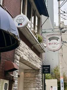 看板は昔のもの（奥）が残っているが、今は2代目のご主人（手前の看板の似顔絵の人）が営んでいる。